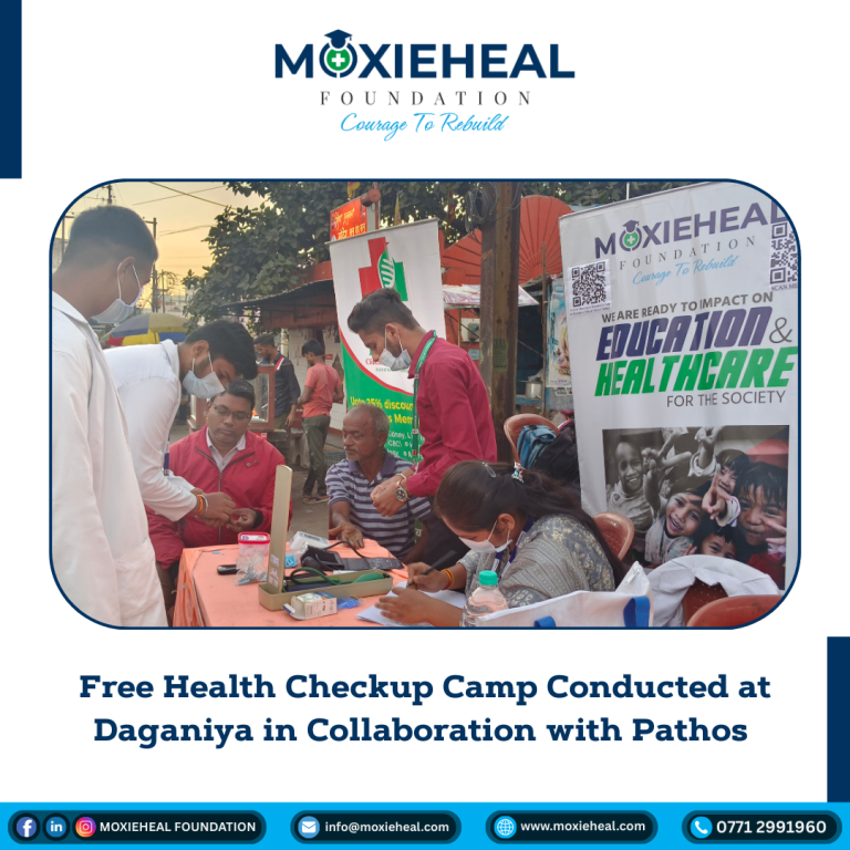 Group of people at a community health camp with staff wearing masks and a banner about education and healthcare in the background